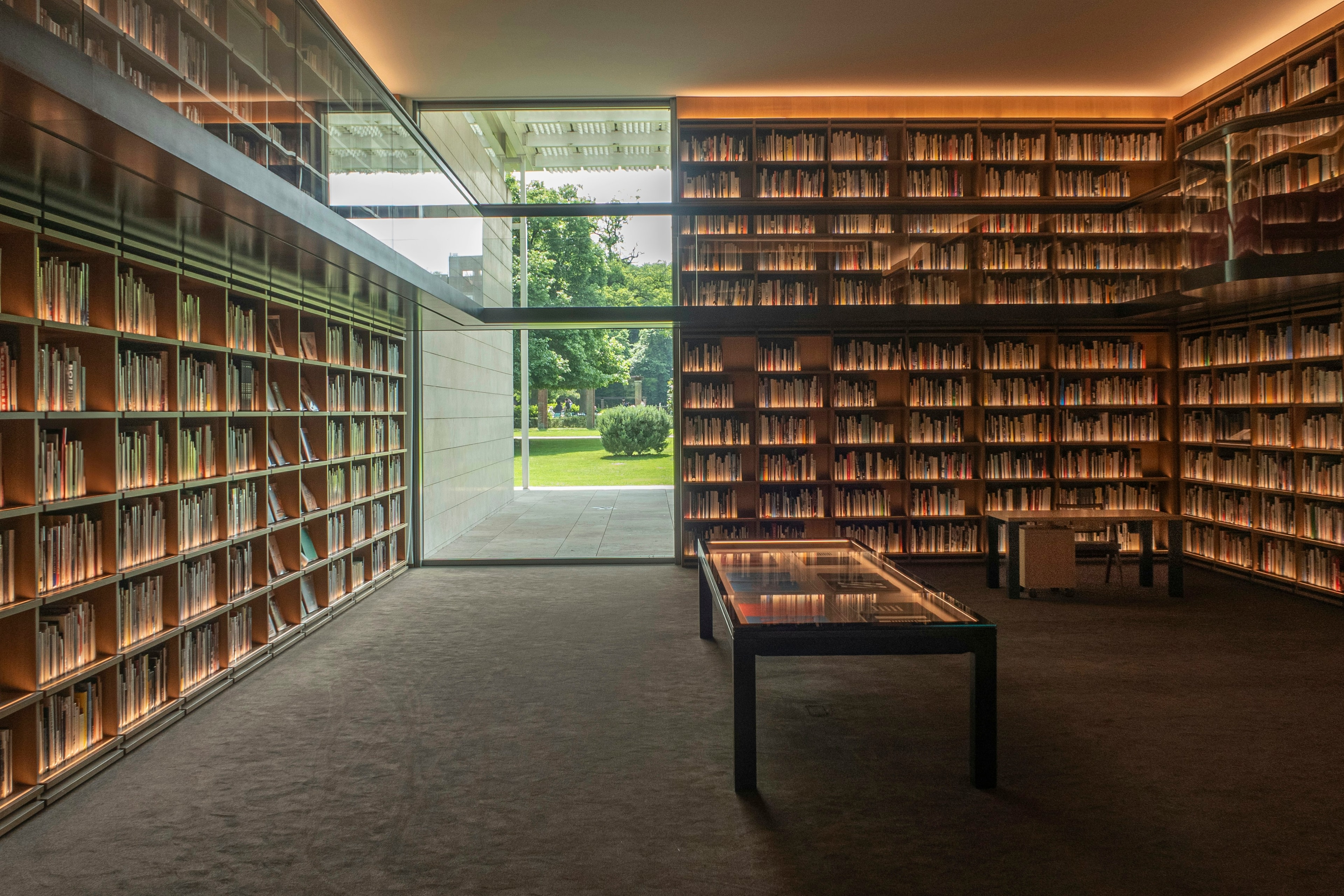 Biblioteca con scaffali a tutta altezza e una grande vetrata sul giardino